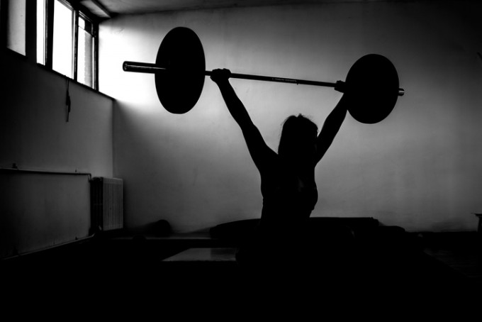 Silhouette of young adult girl doing heavy duty squats in gym with barbell