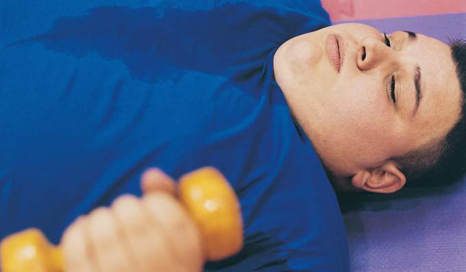 Young Man Lying on an Exercise Mat Lifting a Dumbbell